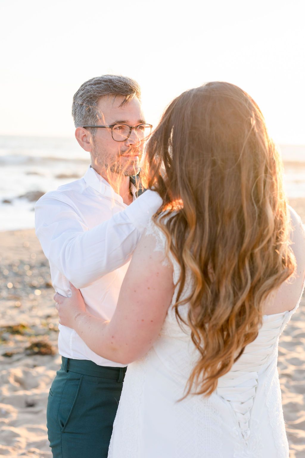 Wedding couple sharing intimate moment during sunset beach photoshoot.