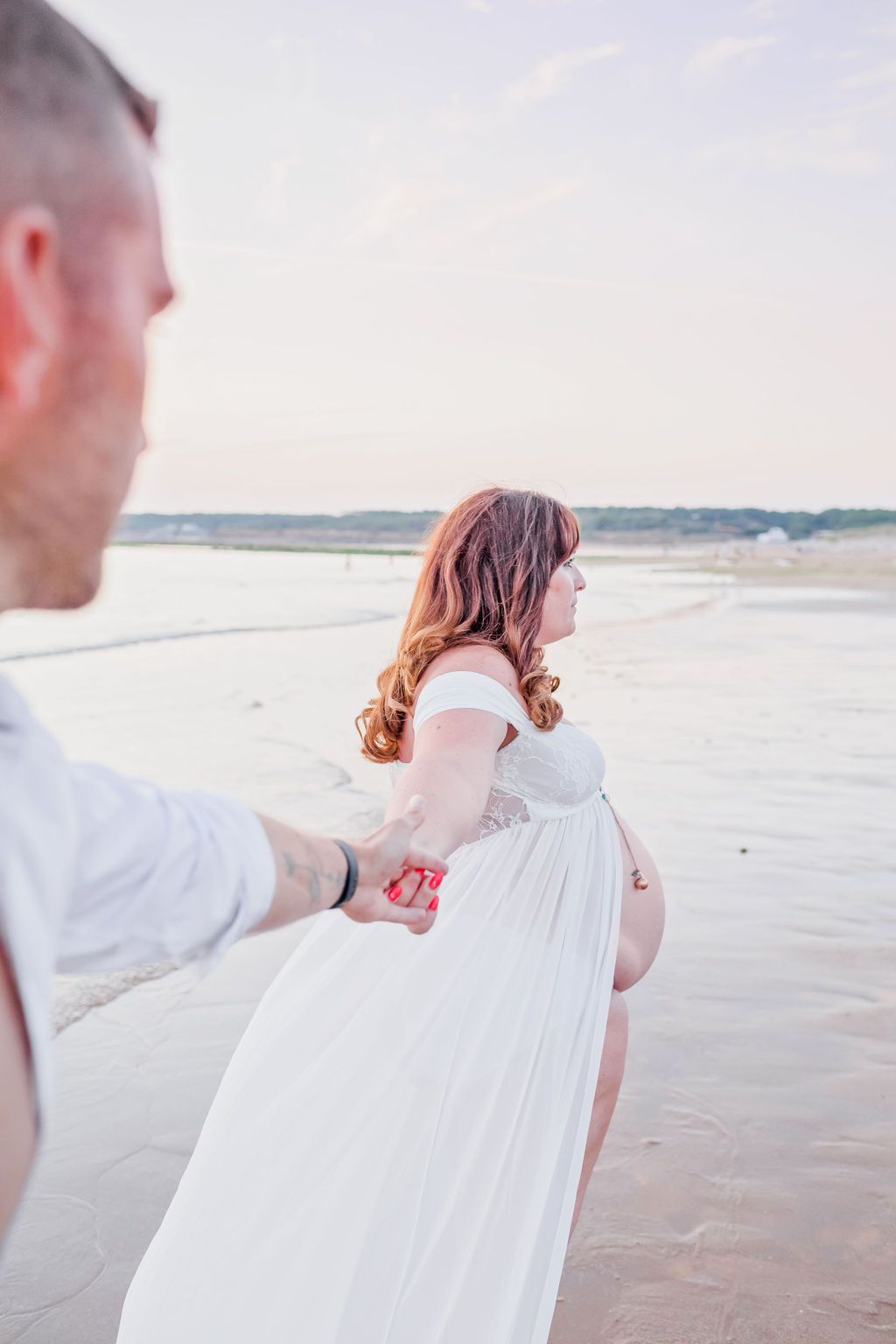 Two people in white clothing embrace while standing on a beach during sunset.