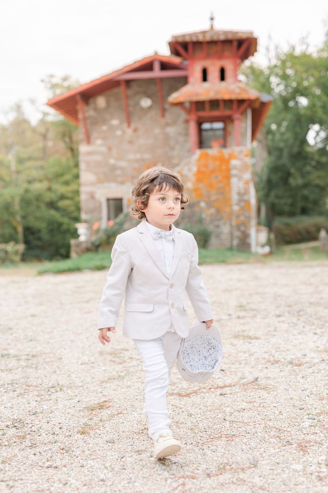 Child in white suit runs playfully near stone buildings.