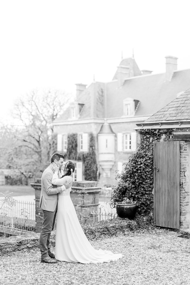 Black and white wedding photo of couple embracing by classic mansion and garden.