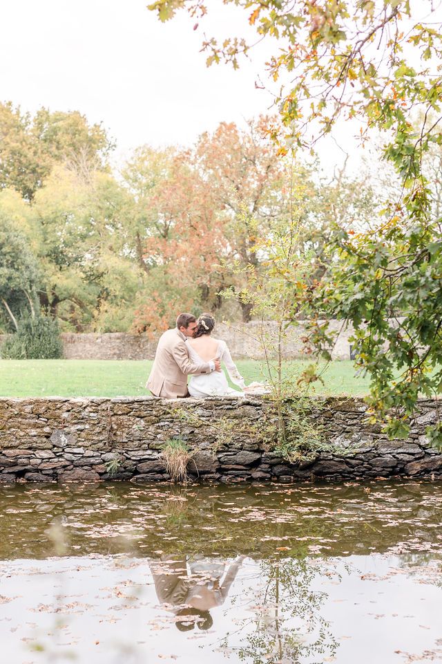 Autumn wedding portraits reflected in still water by rustic stone wall.
