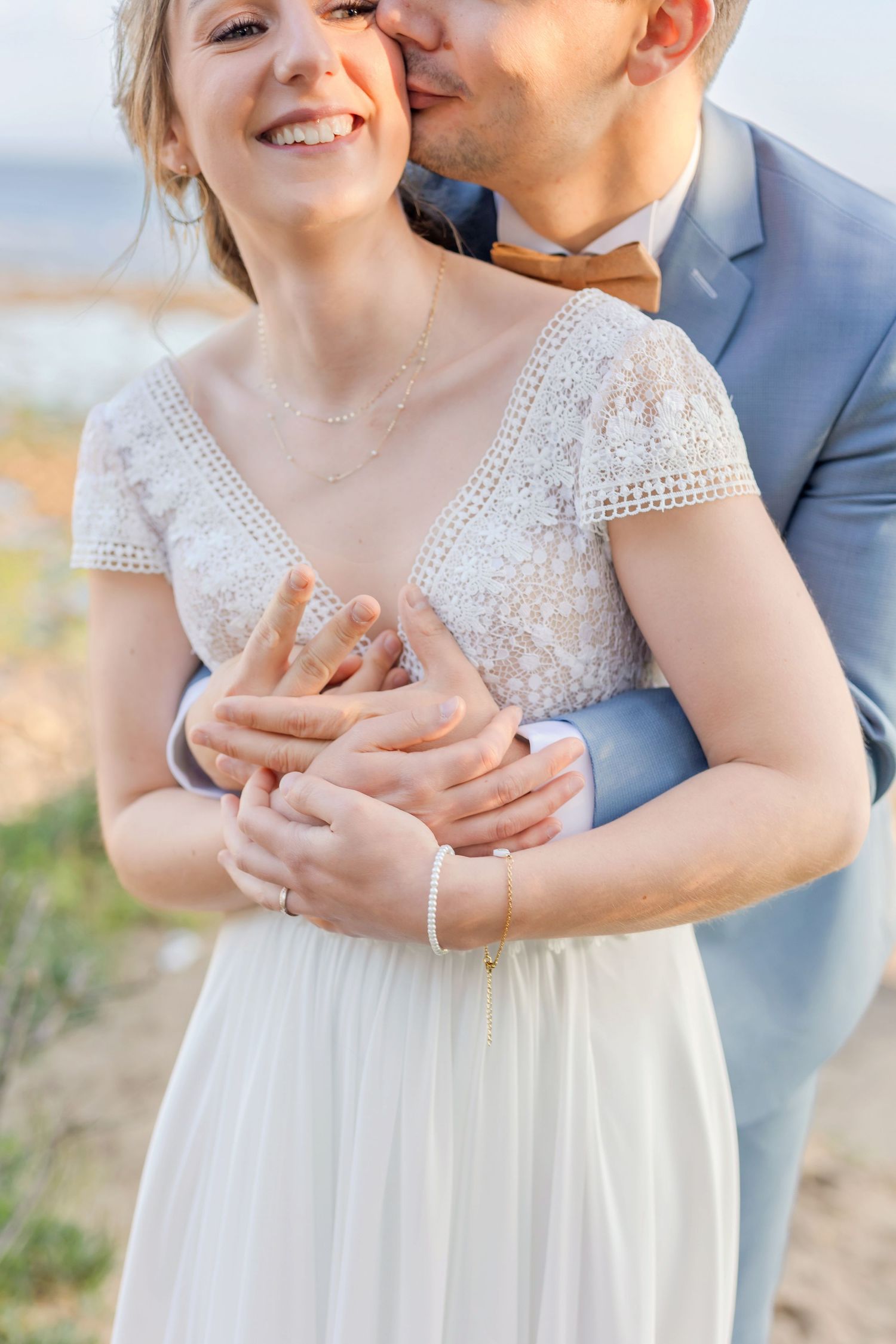 A romantic wedding portrait showing an intimate embrace with the bride wearing a delicate lace dress by the ocean.