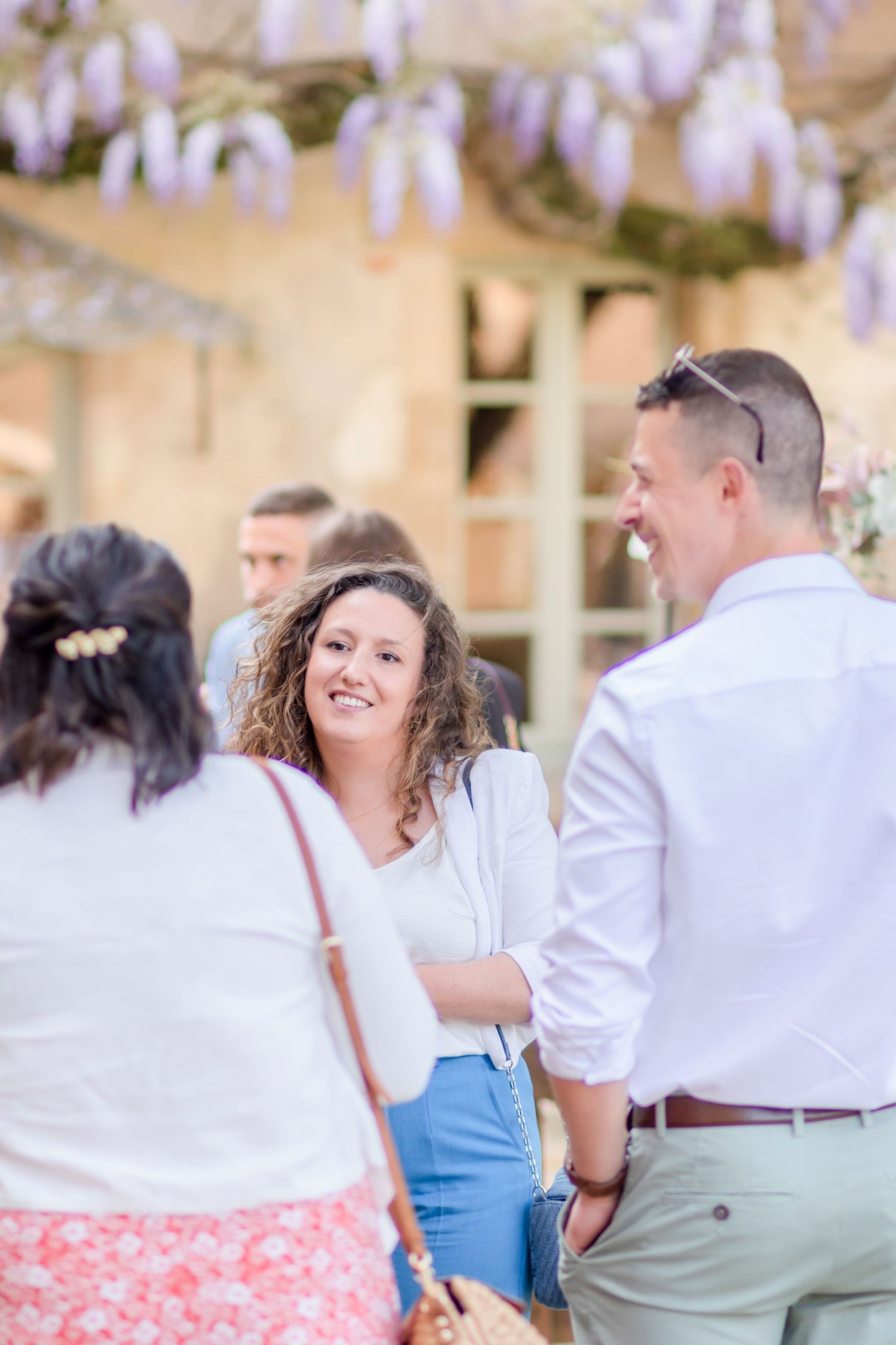 Guests enjoying a casual moment under purple wisteria flowers.