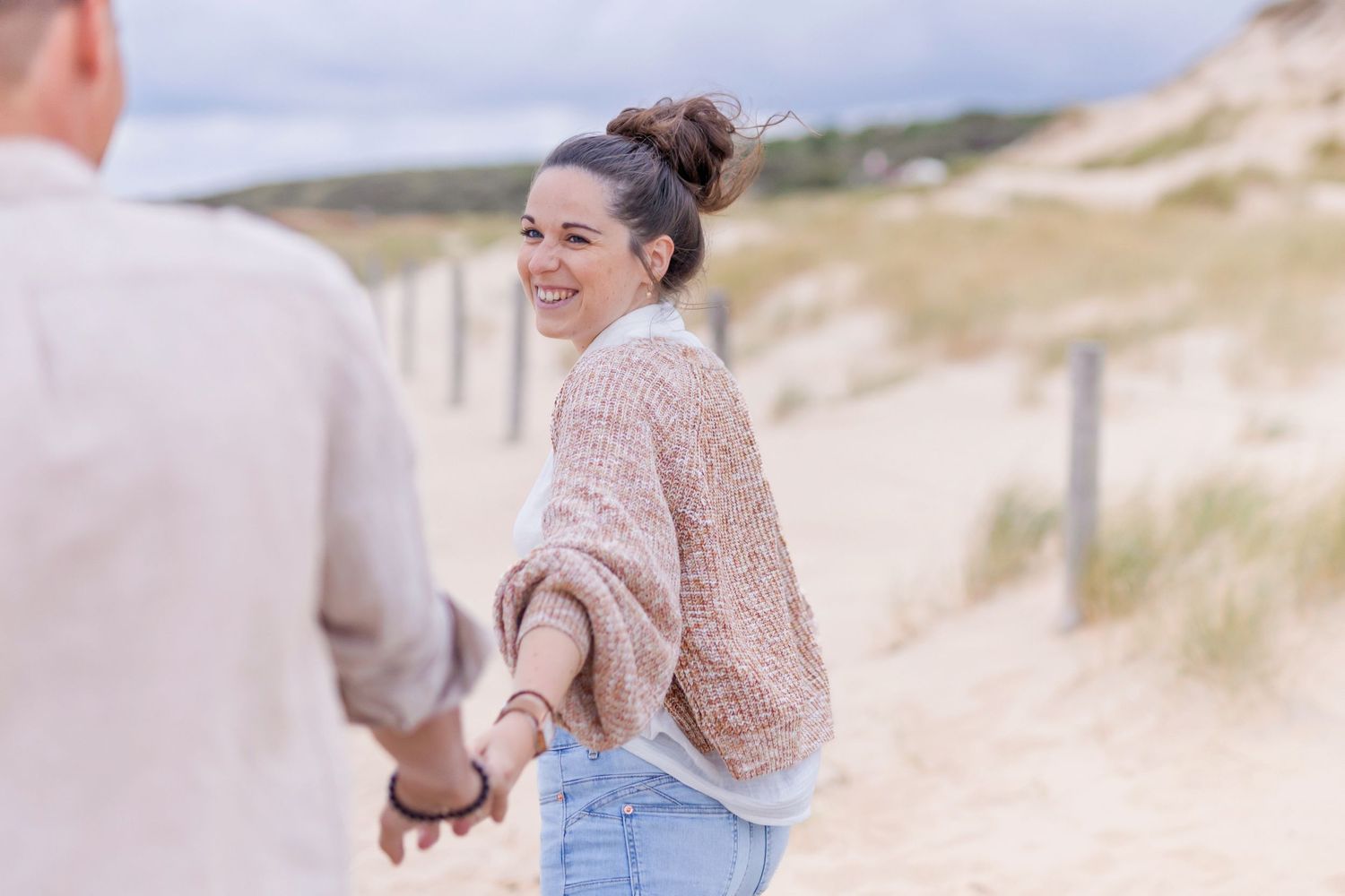 Couple shares joyful moment while walking along coastal sand dunes.