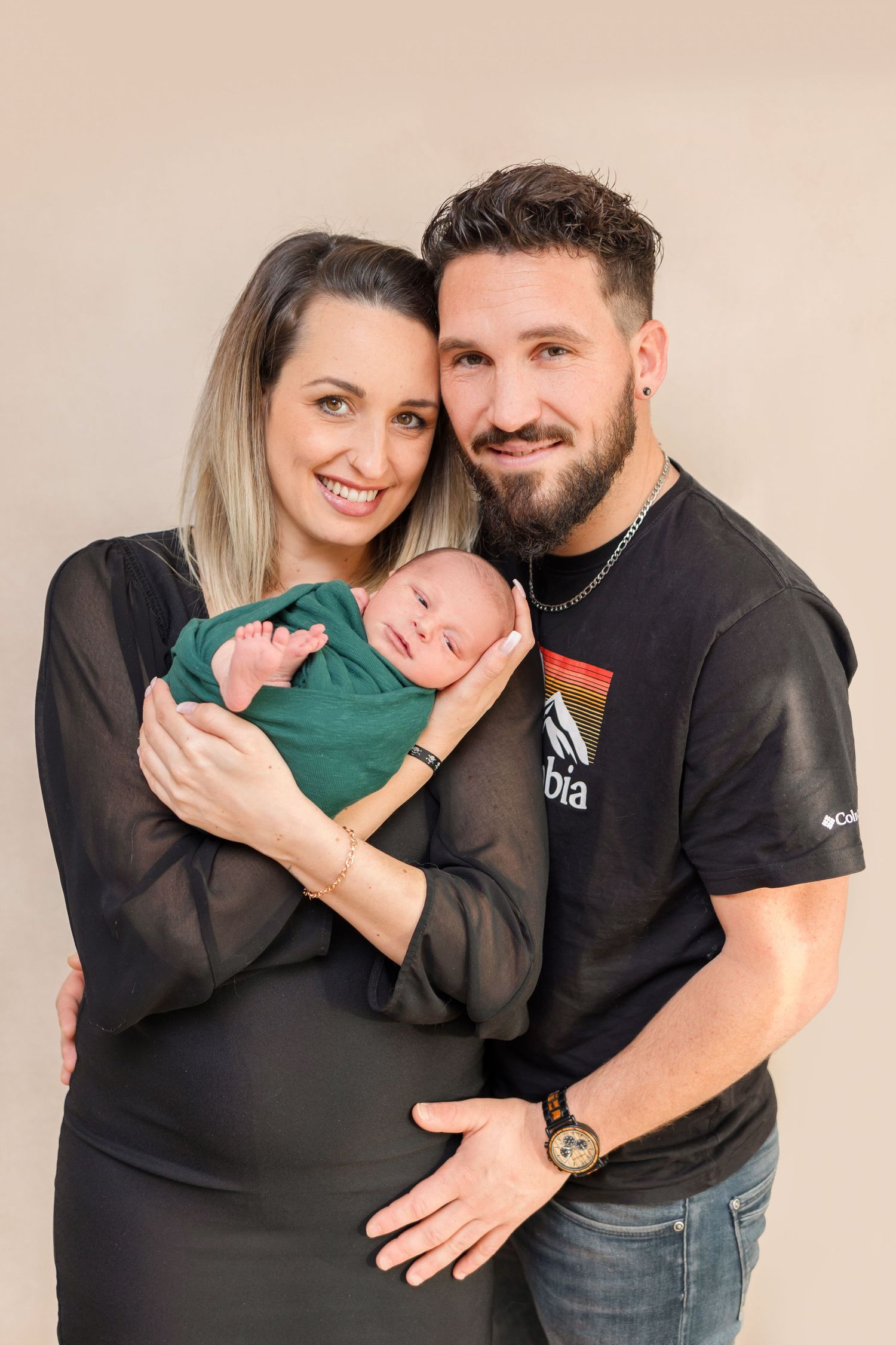 Intimate family portrait with parents cradling their newborn baby in a green outfit.