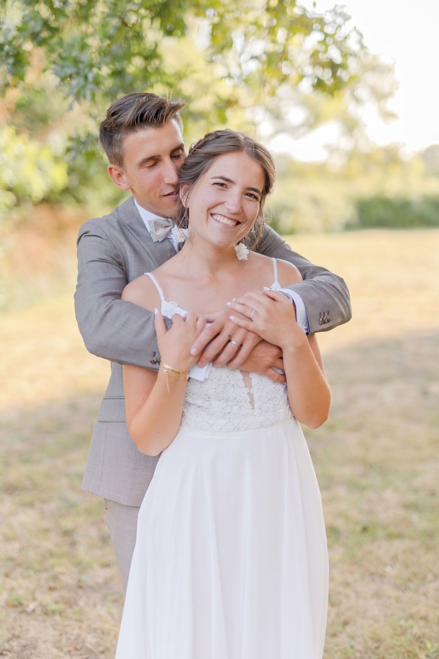 A couple embraces in golden sunlight during an outdoor photoshoot wearing wedding attire.
