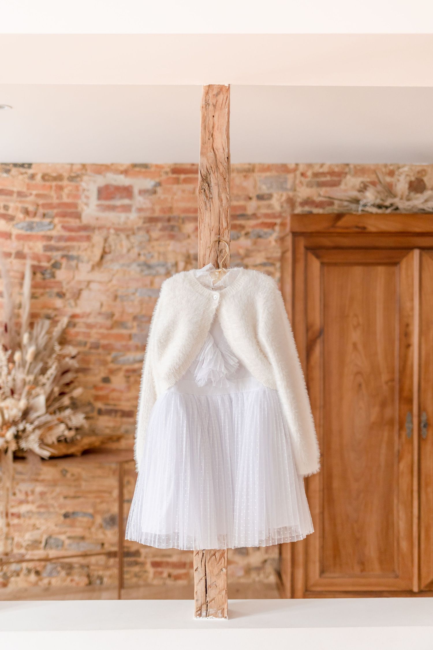White pleated dress with fuzzy cardigan hanging on rustic wooden beam.