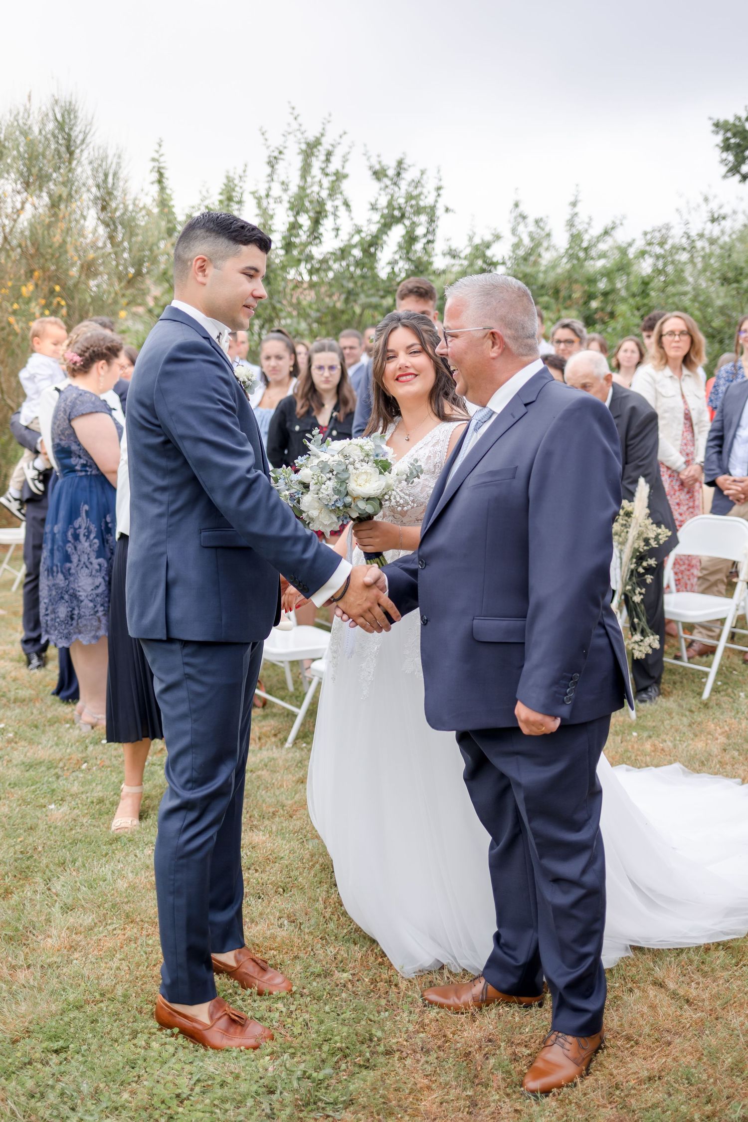 Wedding party in formal attire gathered on grass during outdoor celebration.
