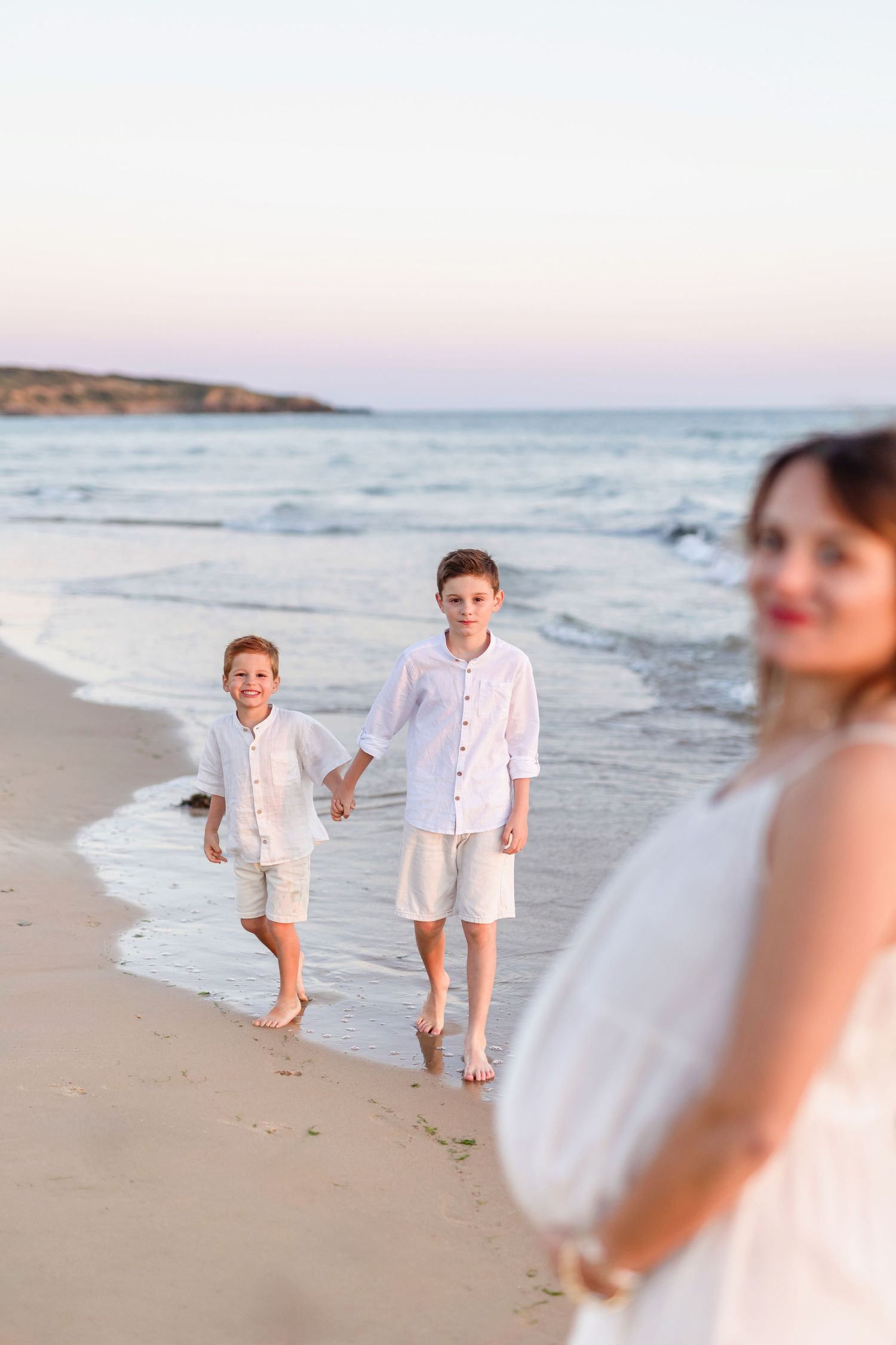 People in white outfits playfully run along the sandy beach at dusk.