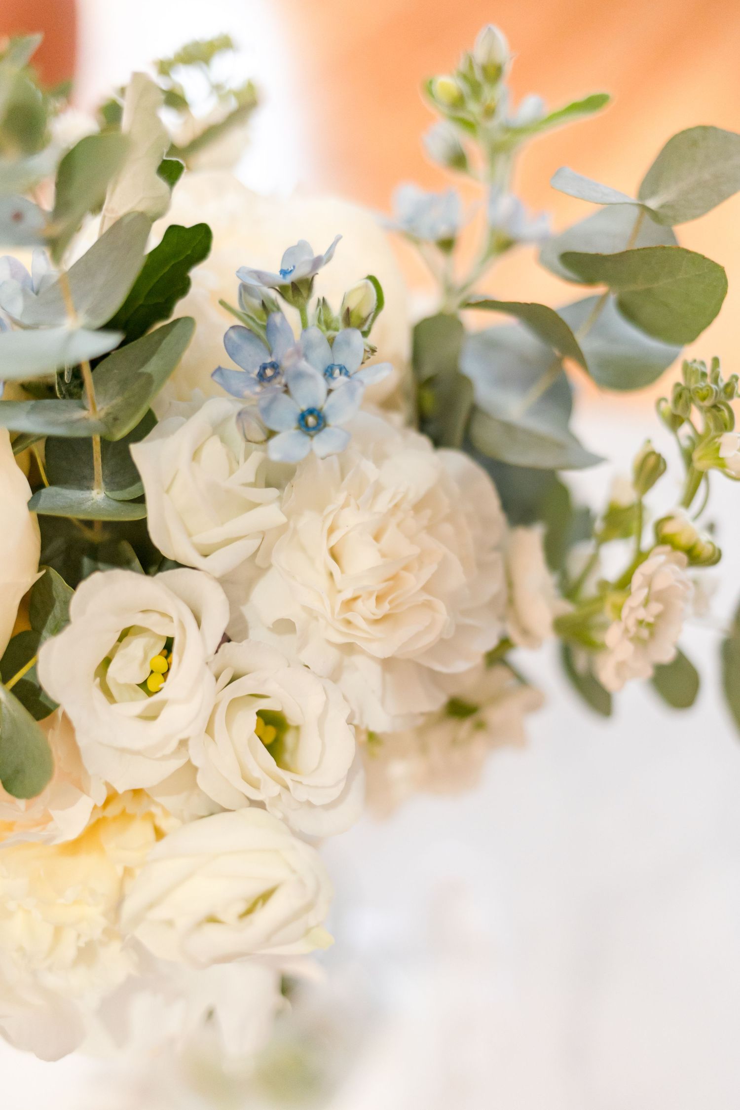 Close-up of white roses and blue flowers with eucalyptus in wedding bouquet arrangement.