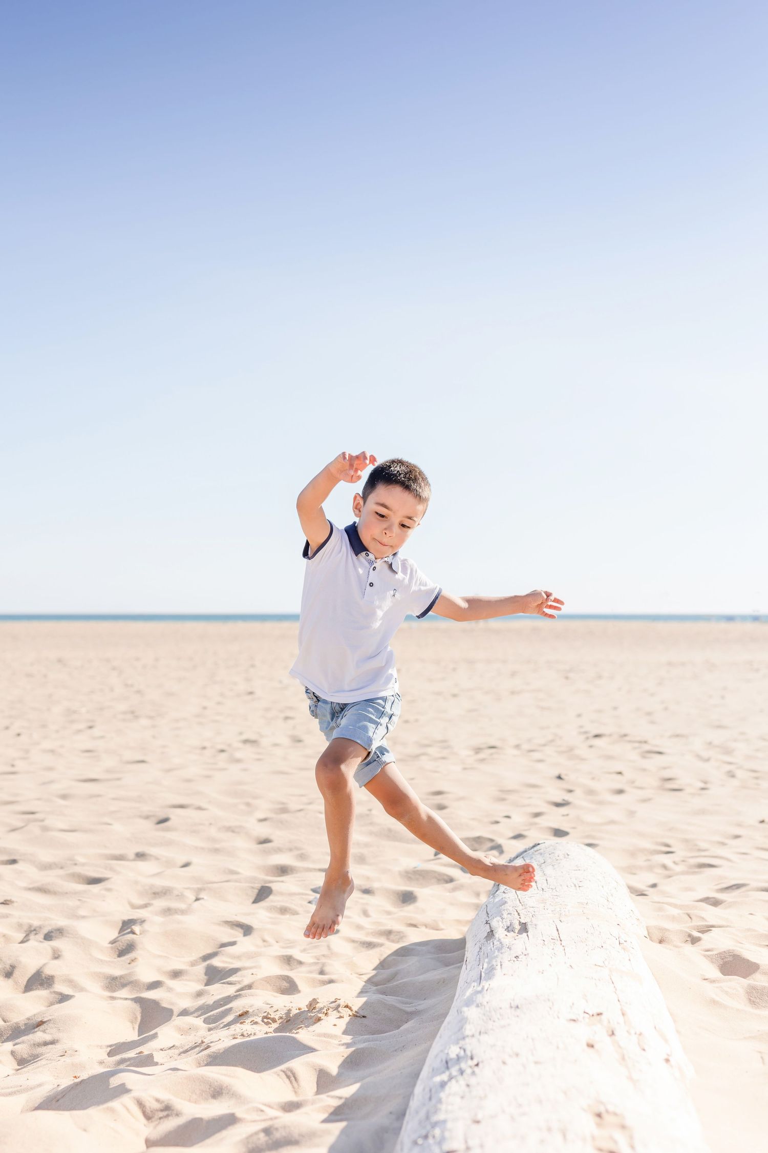 Child balancing and playing on a concrete wall at the beach.