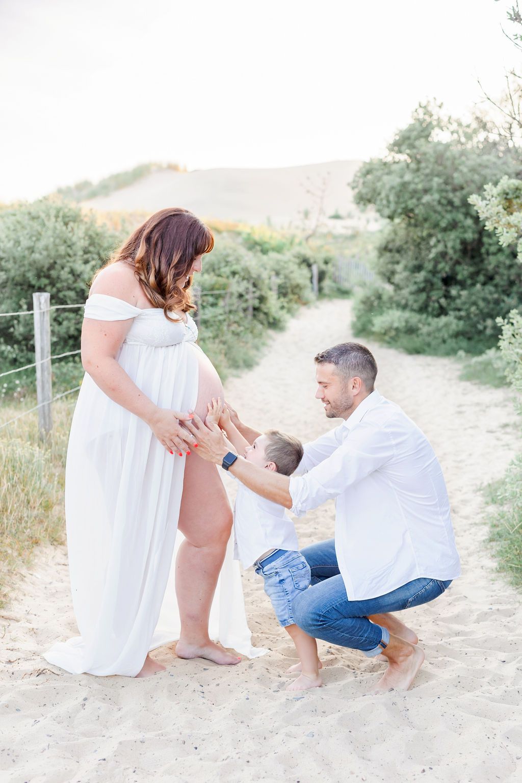 A touching family moment during a maternity photoshoot on a sandy outdoor path.