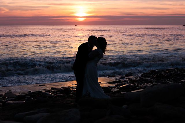 A silhouetted couple embraces against a dramatic orange sunset over the ocean.
