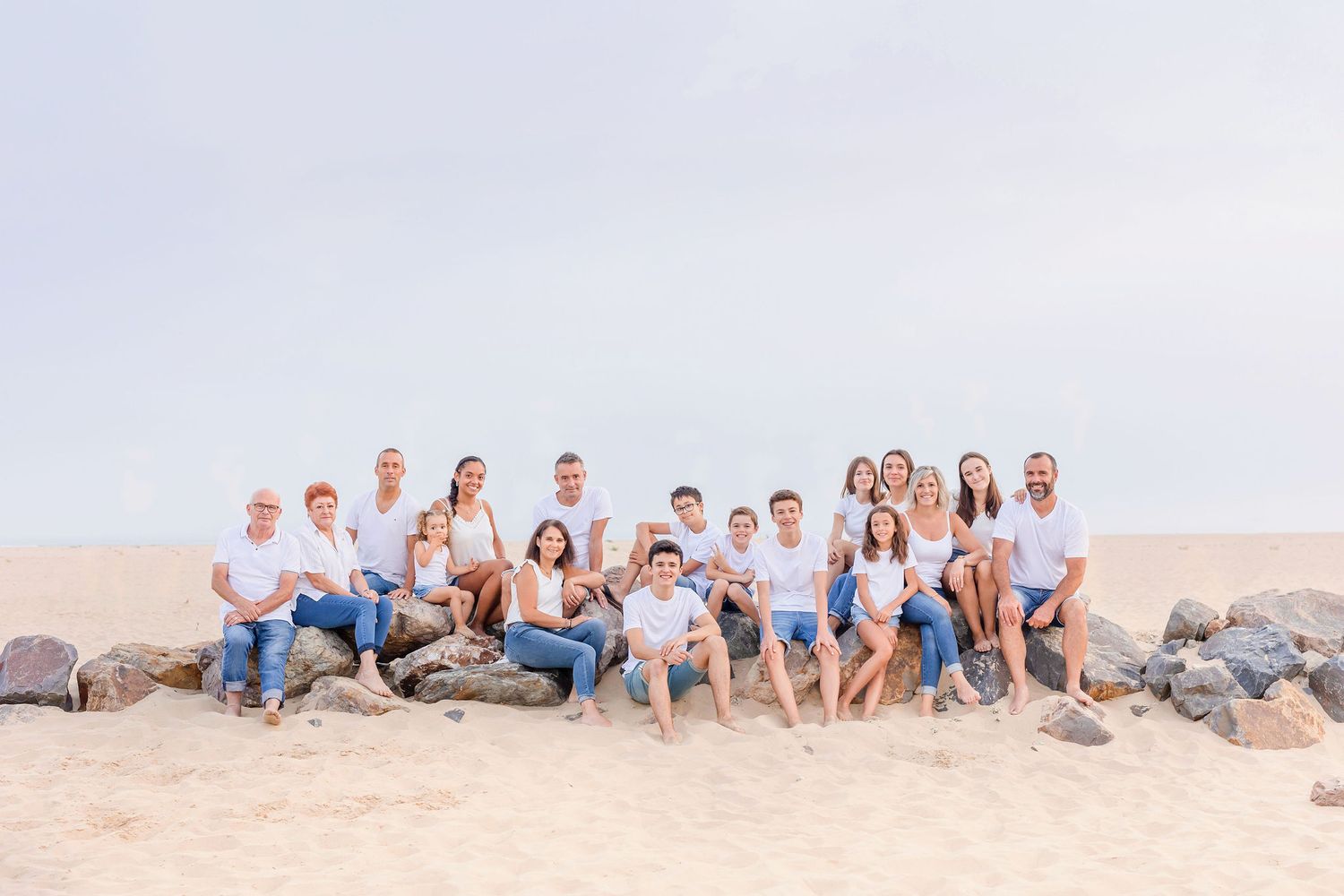 Large family group poses together on a sandy beach wearing coordinated blue and white outfits.