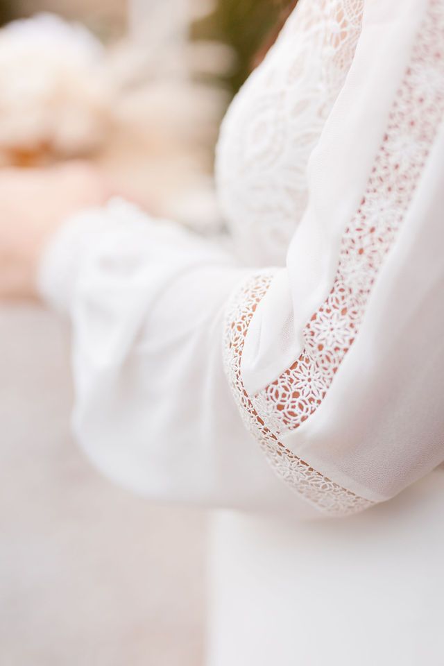 Delicate white lace detail on wedding dress sleeve in soft focus.