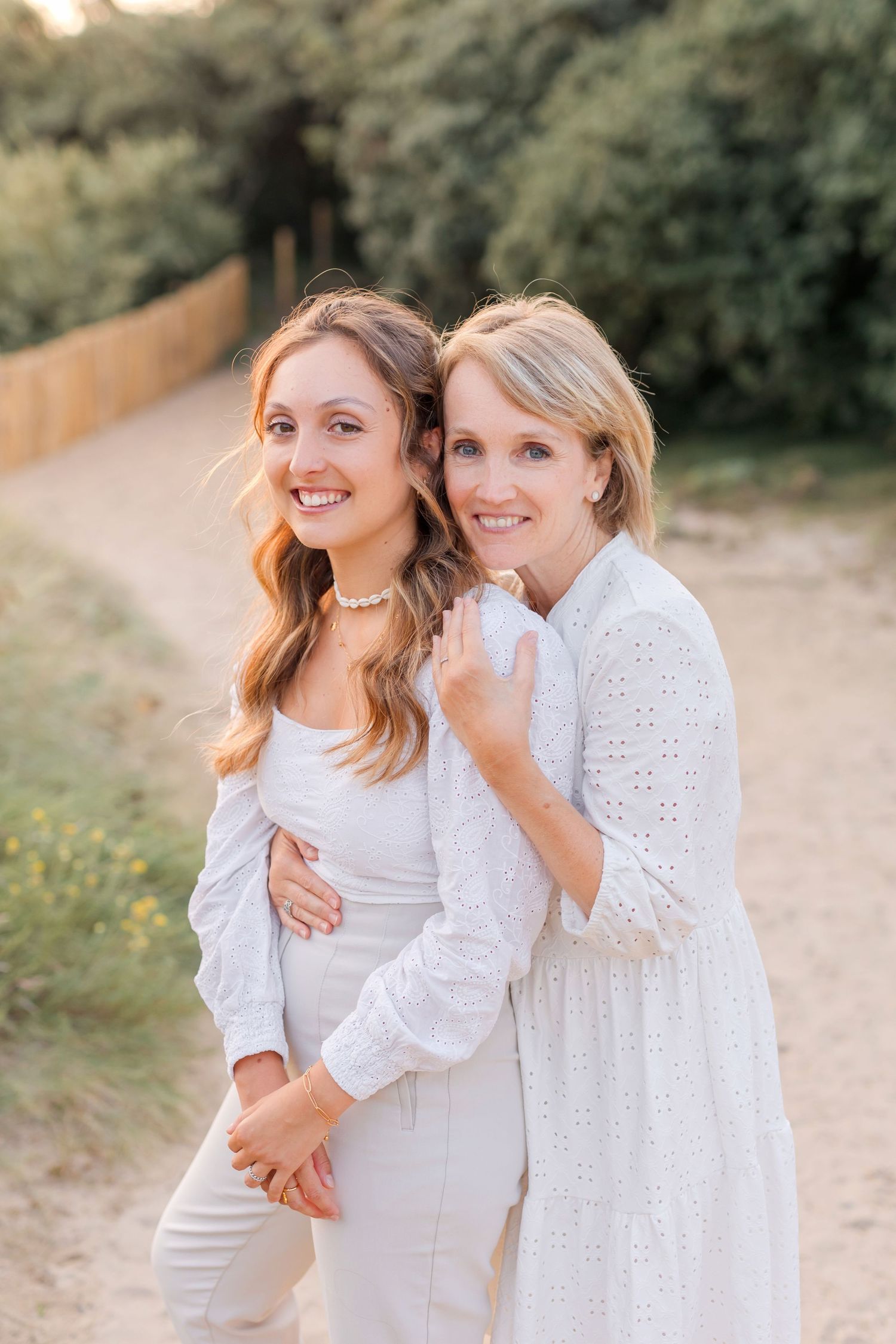 Two people in white outfits pose together on nature path during golden hour.