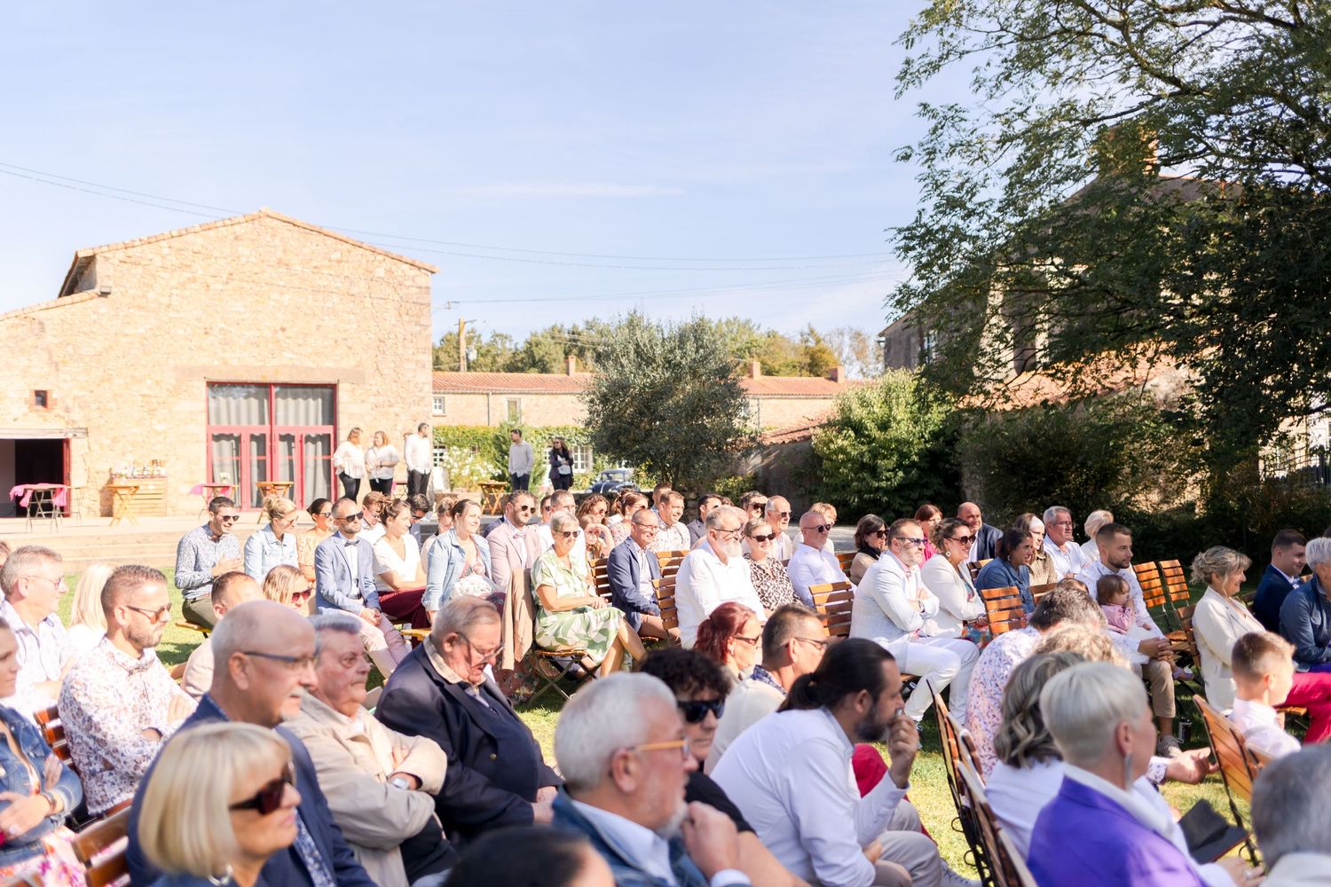 Large group of wedding guests gathered outdoors at rustic venue.