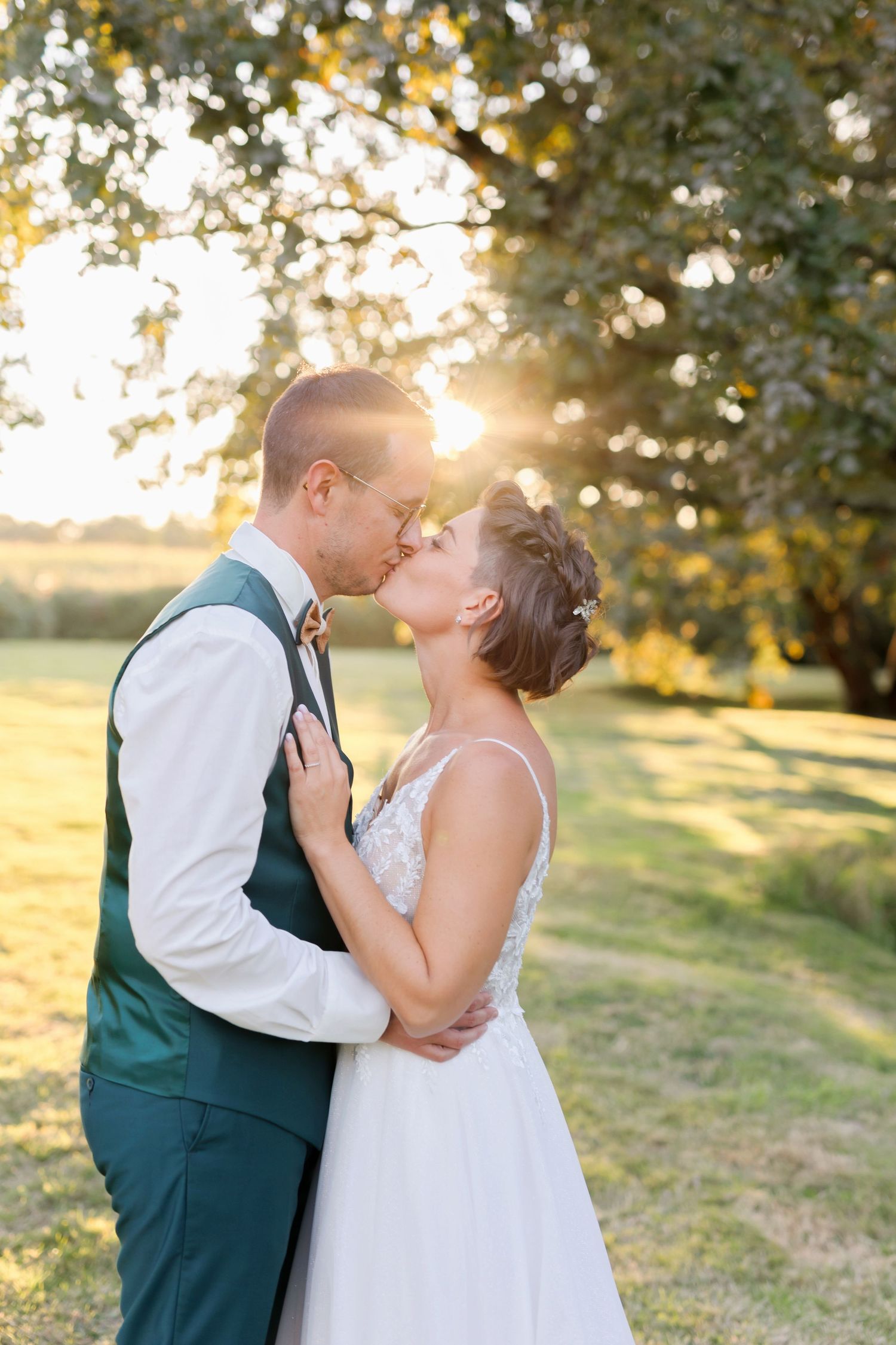 Romantic sunset wedding portrait of couple embracing in a garden with golden backlight filtering through trees.
