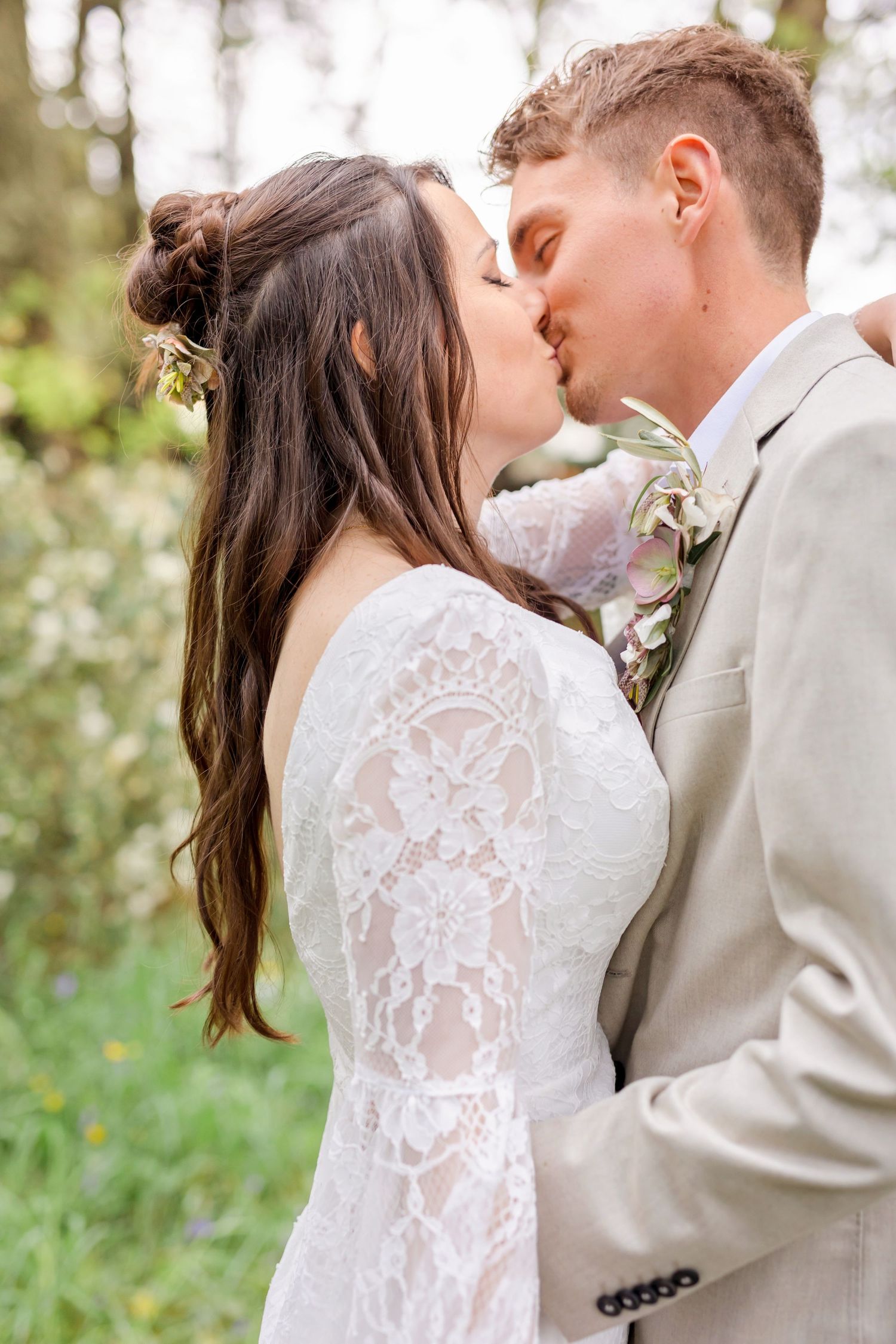 A tender kiss shared between newlyweds in an outdoor garden setting with delicate lace details on the wedding dress.