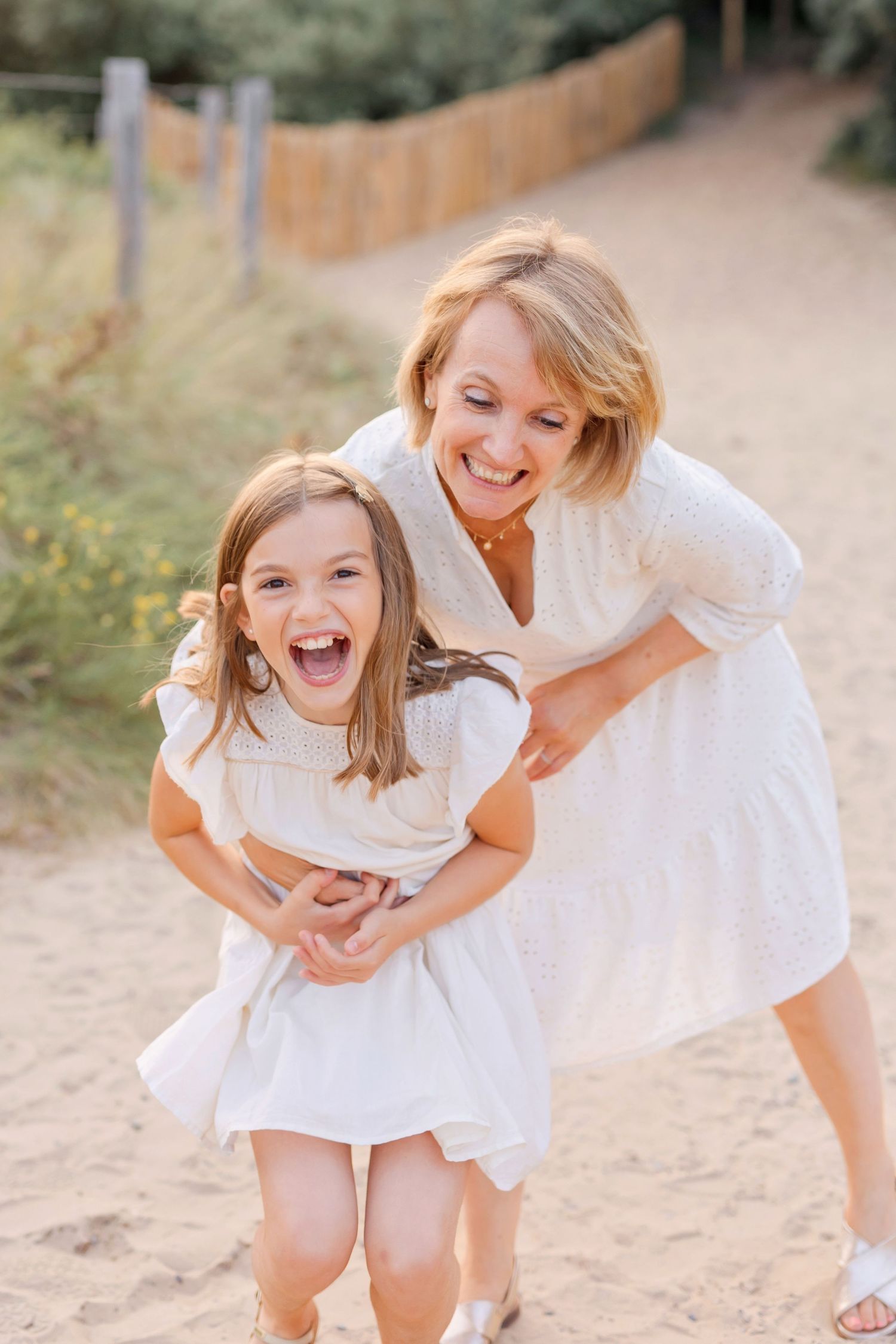 Adult and child in white dresses sharing a playful moment outdoors.
