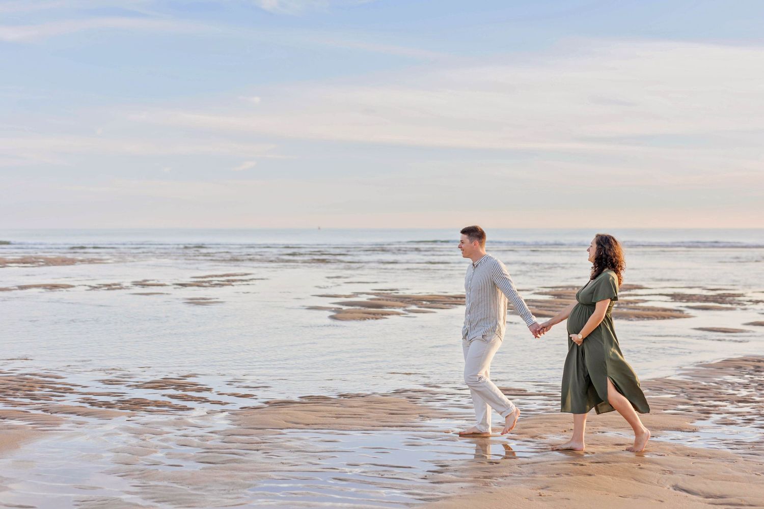 A couple walks barefoot along the beach at sunset, leaving footprints in the wet sand.