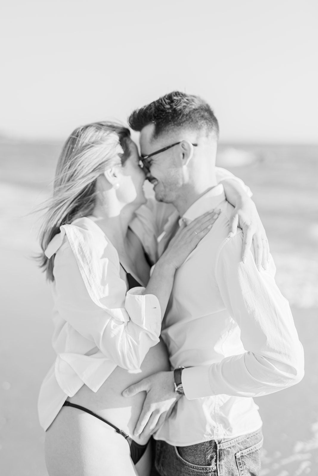 A black and white photo series showing a romantic couple in white shirts embracing on the beach.