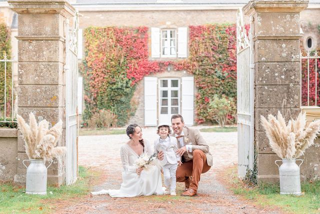 Family photo framed by stone pillars with pampas grass decorations at French estate entrance.