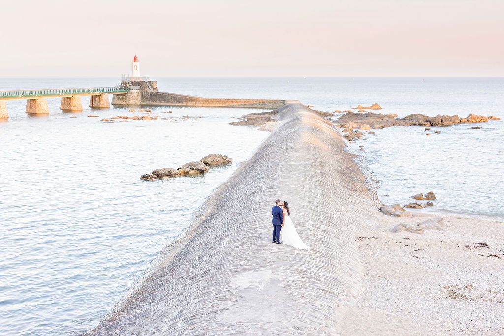 Ethereal coastal wedding scene with distant figures on a curved beach peninsula.