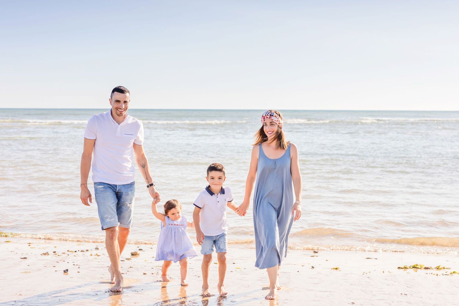 Family of four taking a casual stroll along the shoreline on a bright beach day.