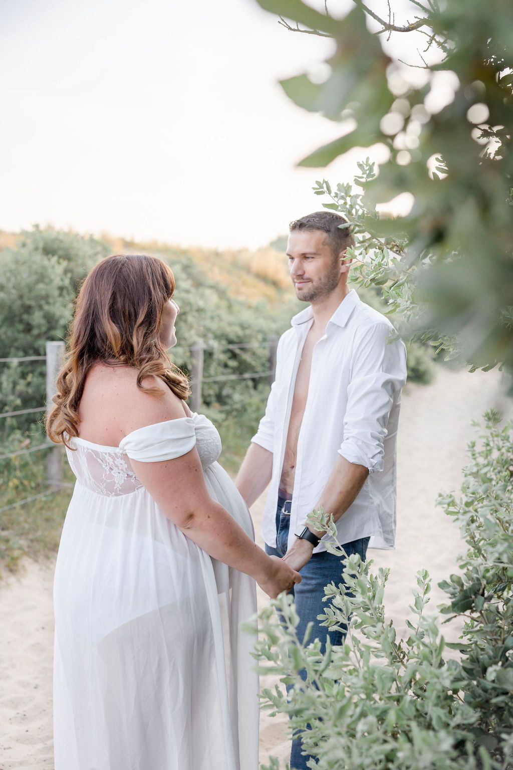 A peaceful maternity portrait of a couple holding hands on a nature trail at sunset.