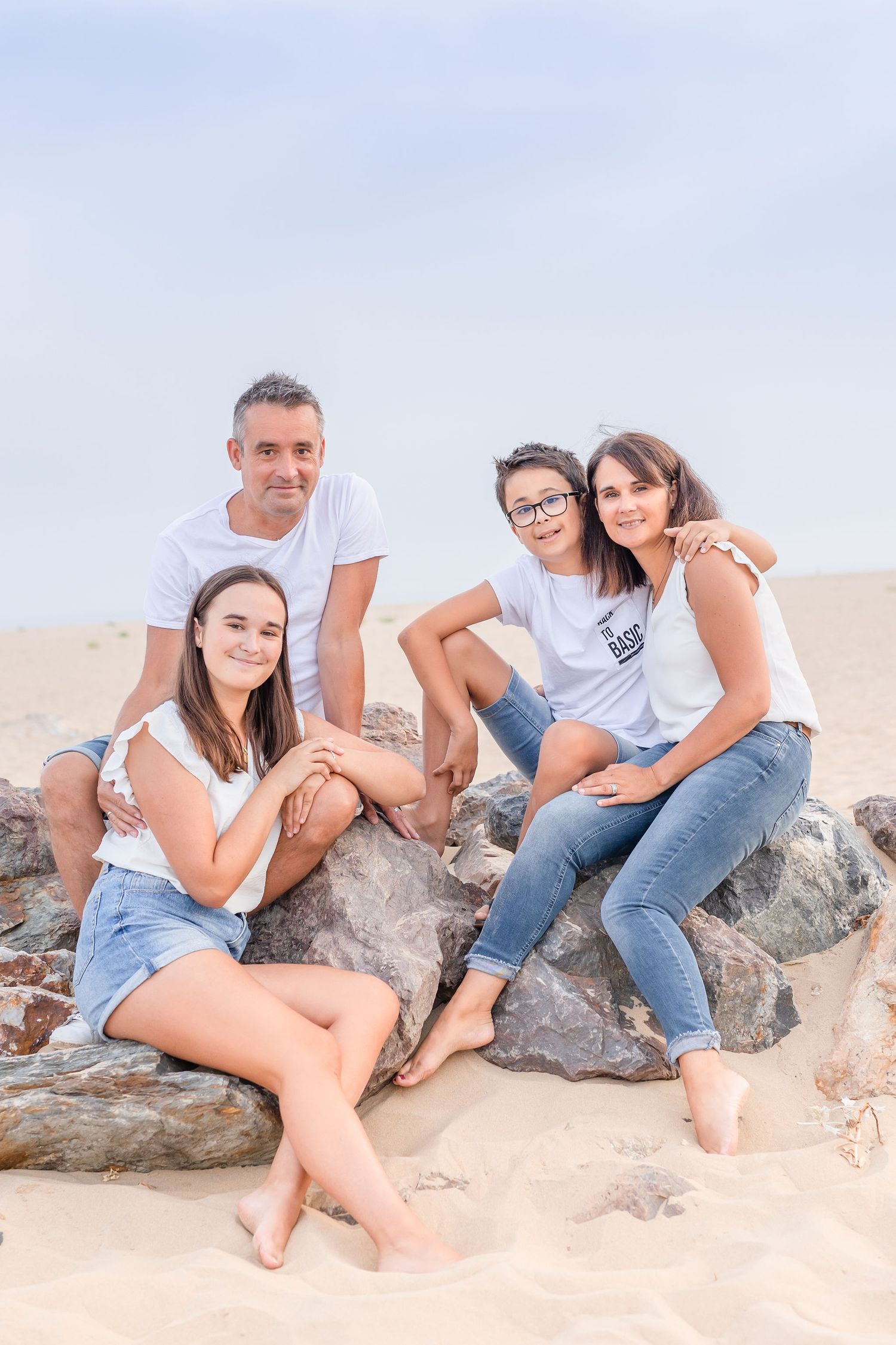 Family members sit casually on rocky beach formations during an outdoor photo session.