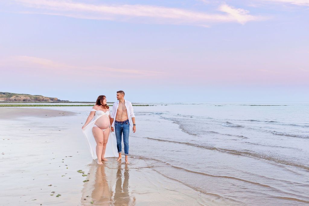 Two people walking together on wet sand at the beach during golden hour.