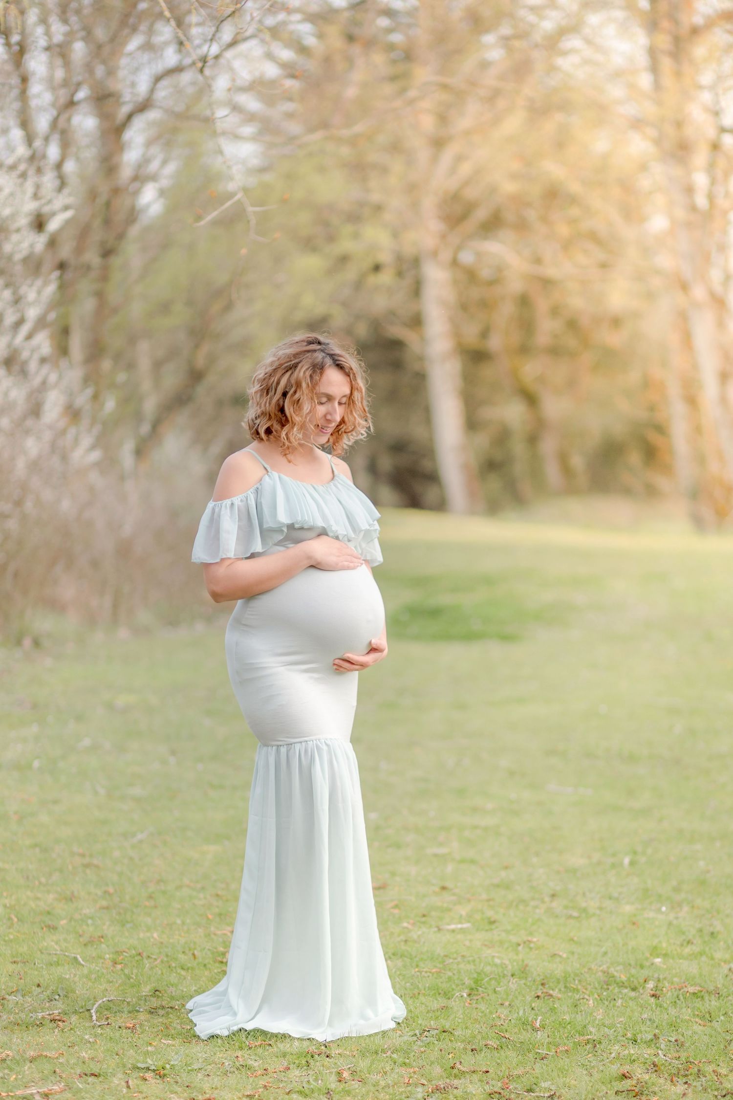 Expecting mother in flowing blue dress poses in spring garden setting.