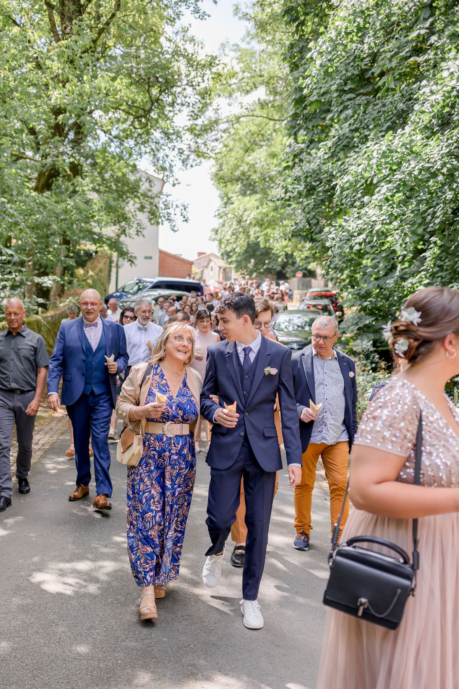 Wedding guests mingling on tree-lined path during outdoor reception.