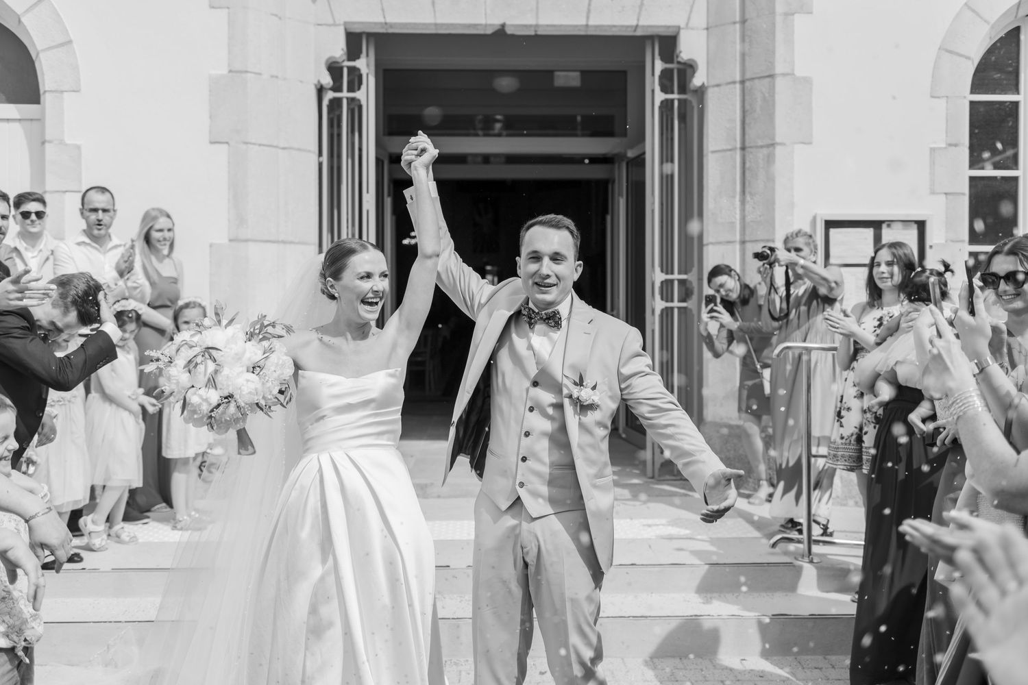 Celebratory exit from church with guests cheering in black and white photography.