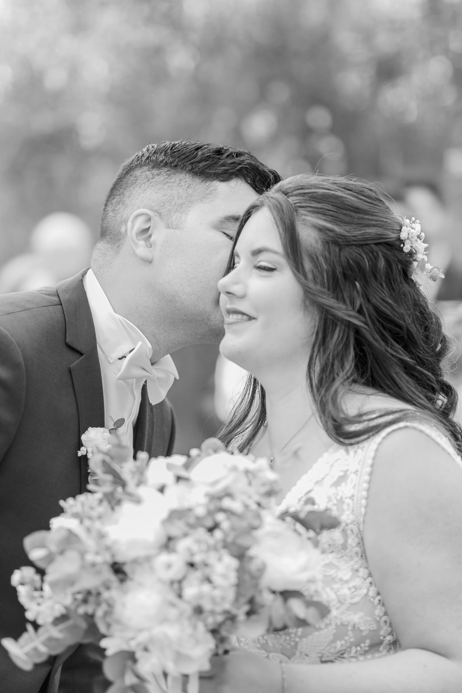 Romantic black and white portrait of couple holding bouquet in garden setting.