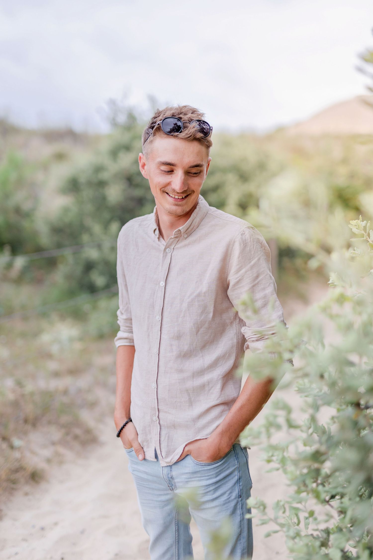 Person in light colored button-down shirt smiling outdoors with sunglasses on head.
