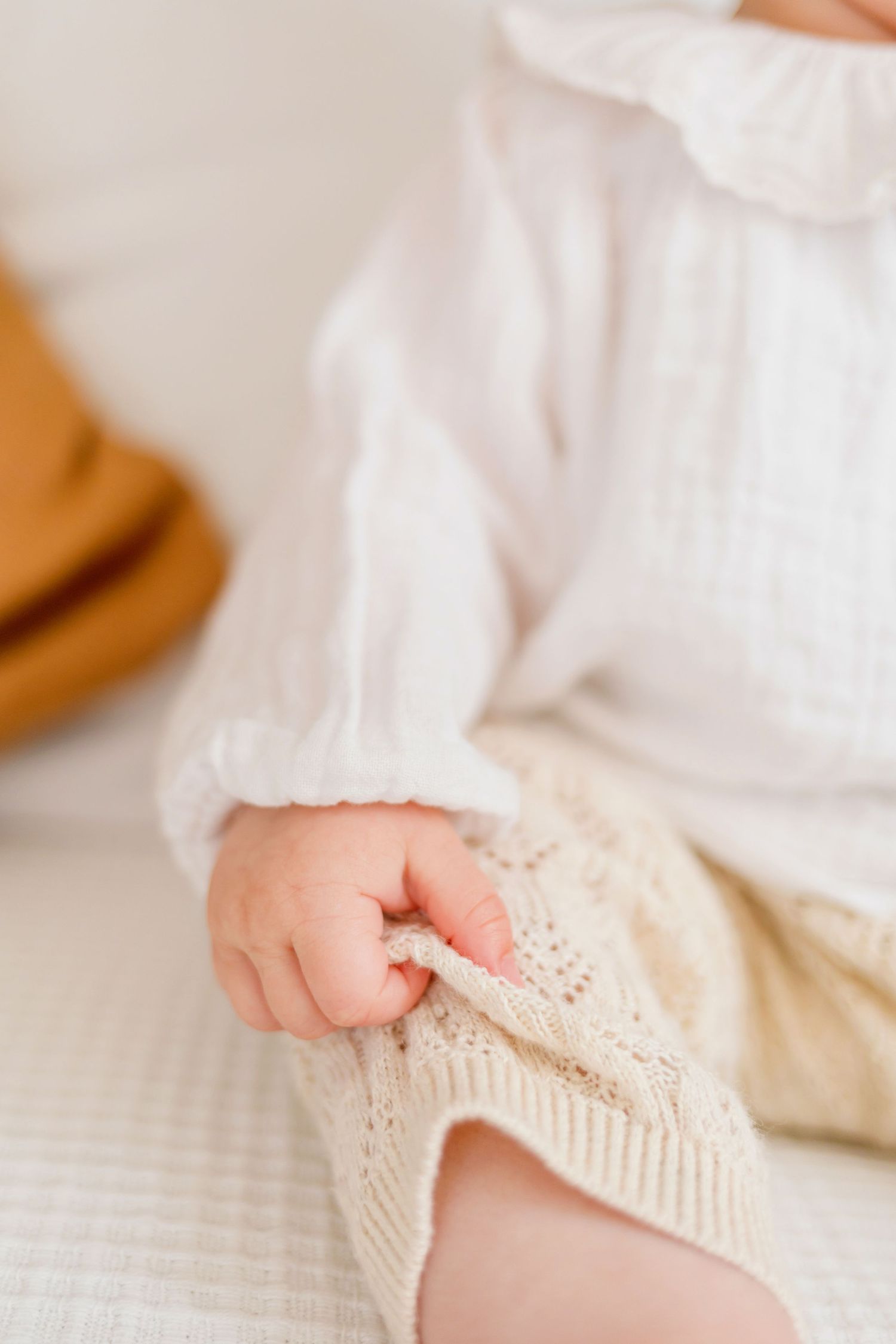 Close-up of tiny baby feet wearing cream colored knit booties on white bedding.