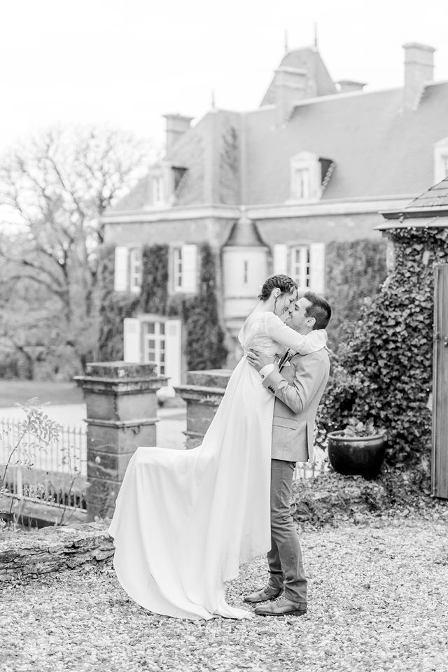 Black and white portrait of newlyweds in romantic embrace by vintage mansion.