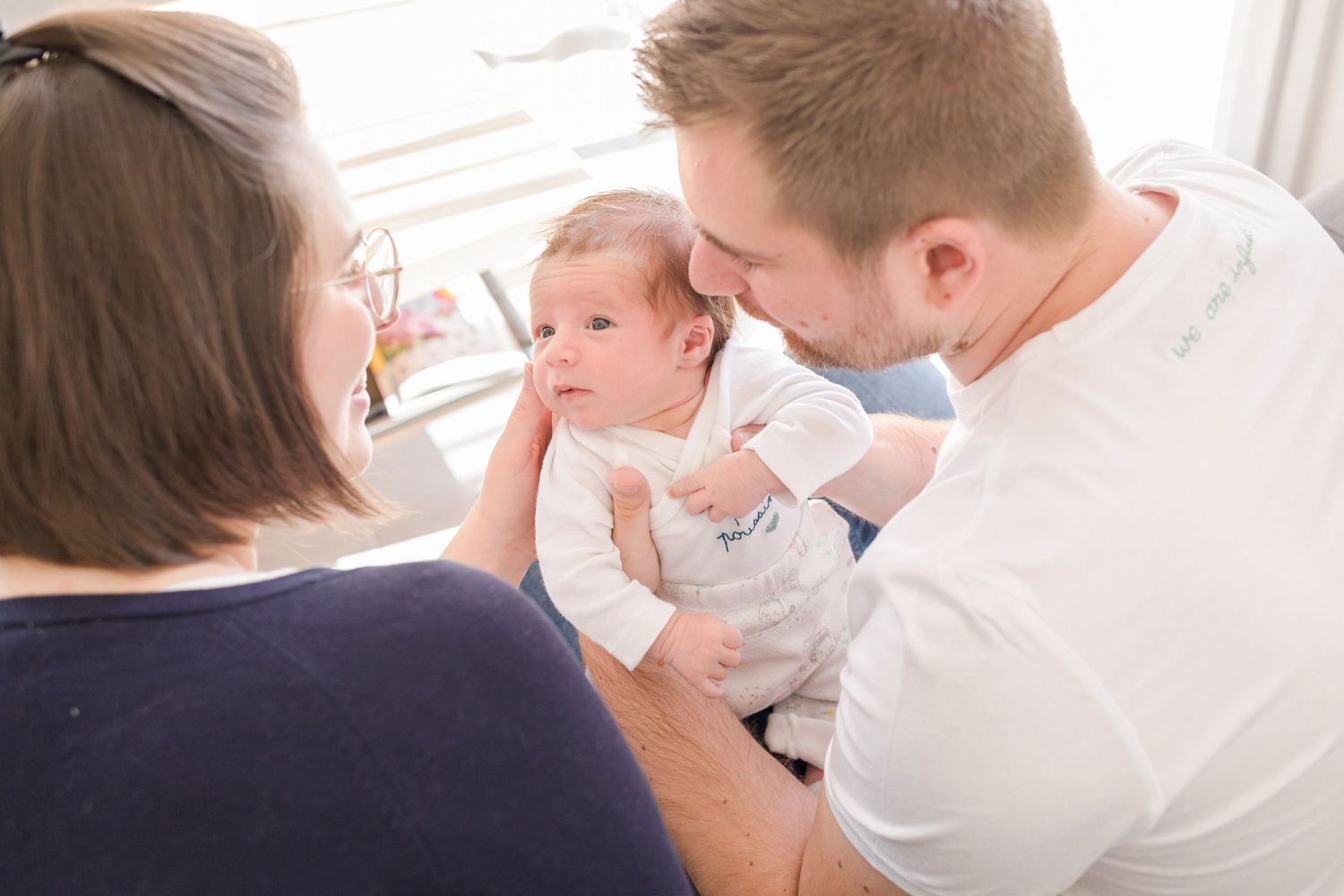 A tender moment with a baby in white clothing being held and cared for on a couch.