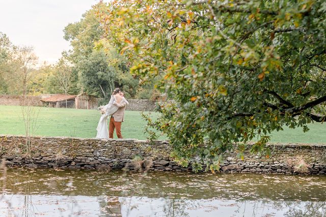 A couple in wedding attire stands by a tranquil pond surrounded by autumn trees in a romantic garden setting.