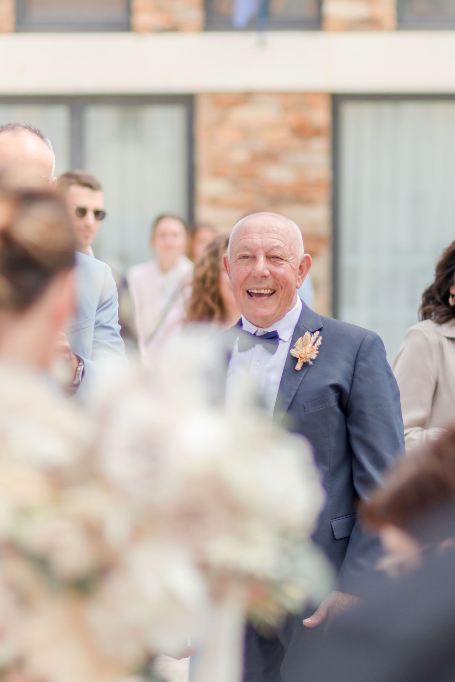 Guest in navy suit smiles while mingling at outdoor wedding reception.