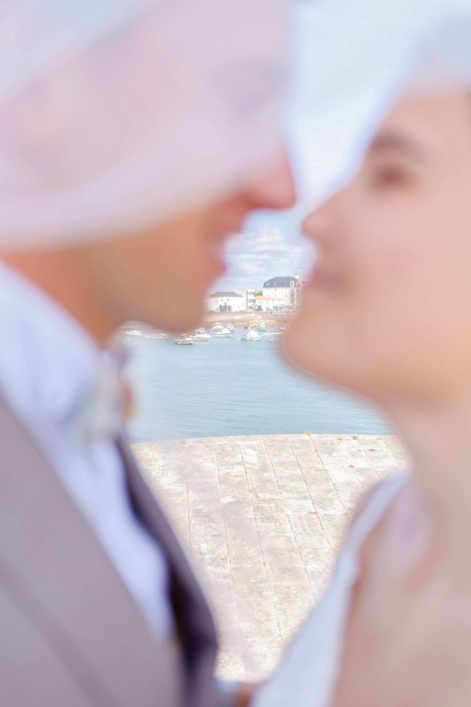 Romantic waterfront wedding photo captured through delicate white veil with soft blur effect.