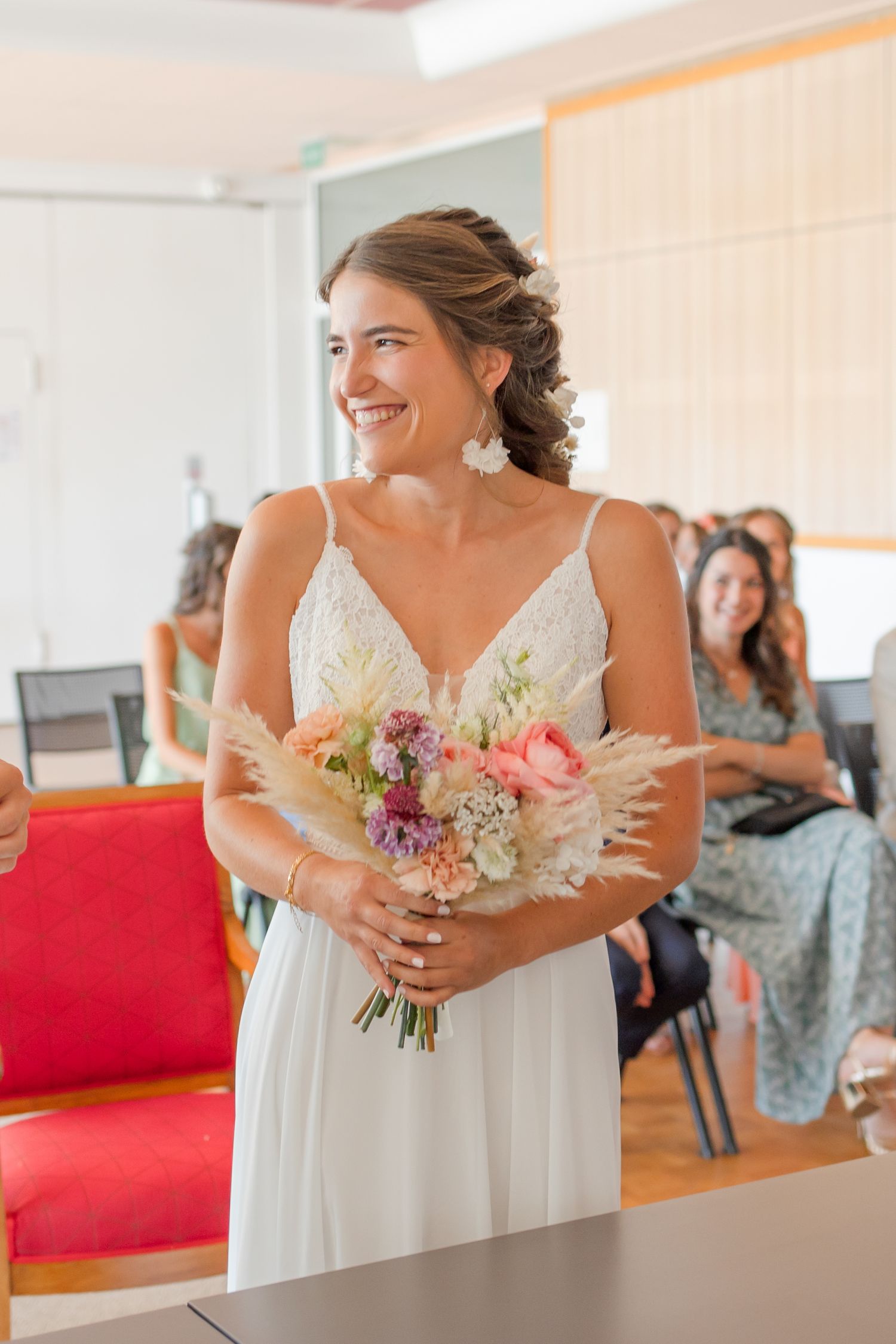 Bride holding colorful bouquet in white dress during indoor wedding ceremony.
