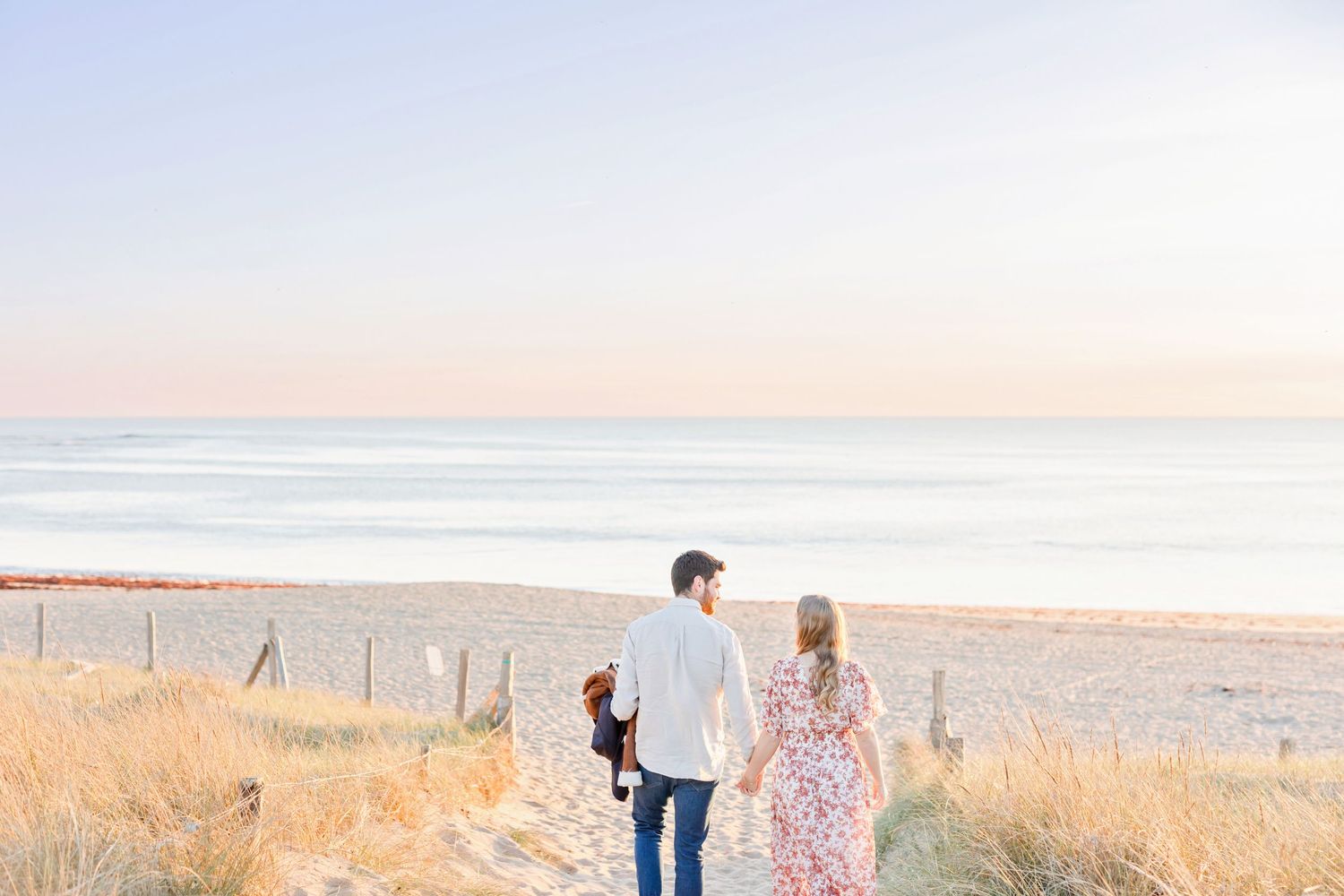 A couple walks hand in hand along a coastal path with ocean views at dusk.
