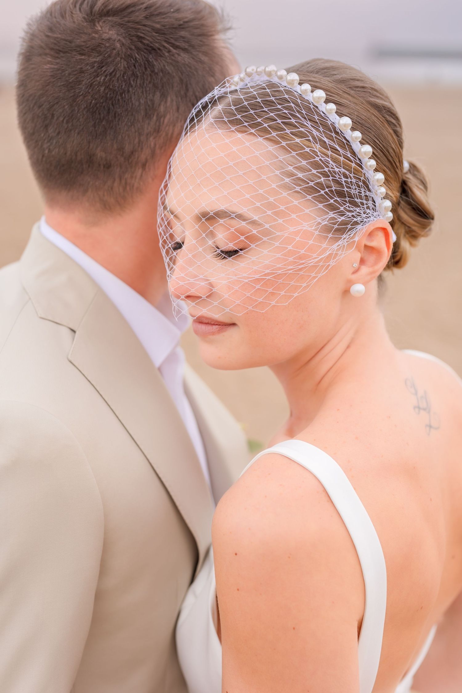 A serene portrait of a bride wearing a pearl-adorned veil against a soft background.