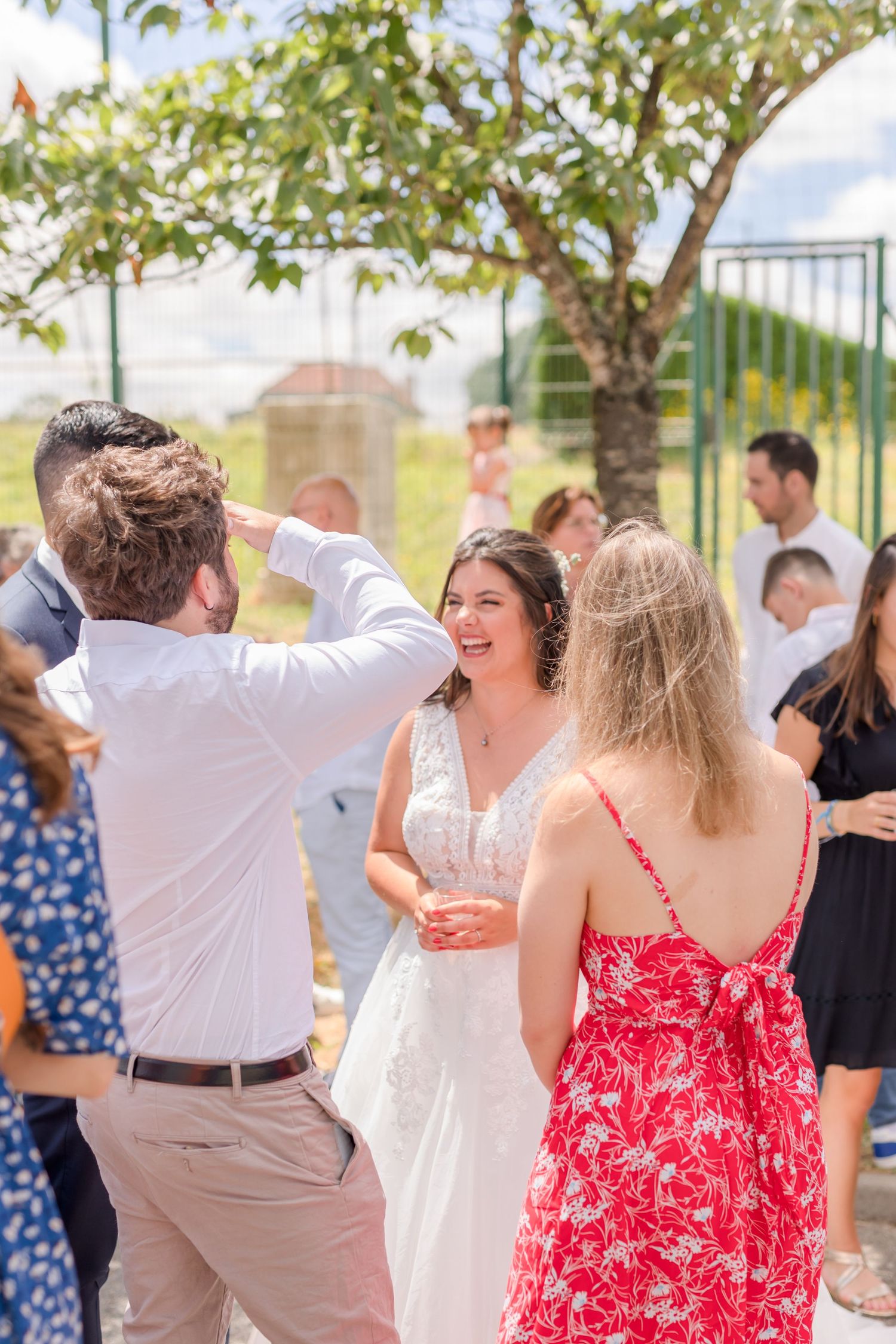 Wedding celebration with guests dancing outdoors under a leafy canopy.