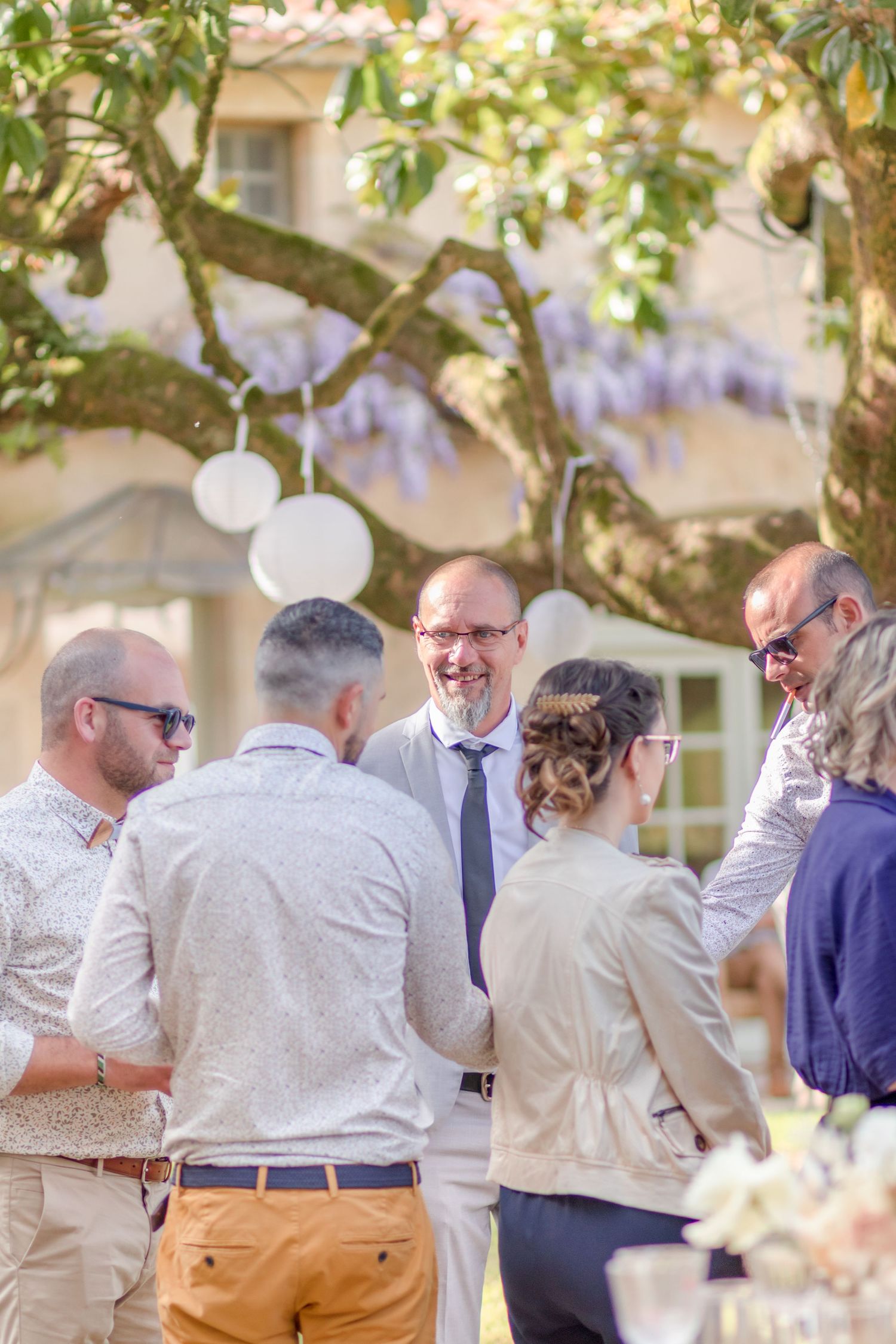 Wedding guests mingling under a canopy of green leaves and wisteria.