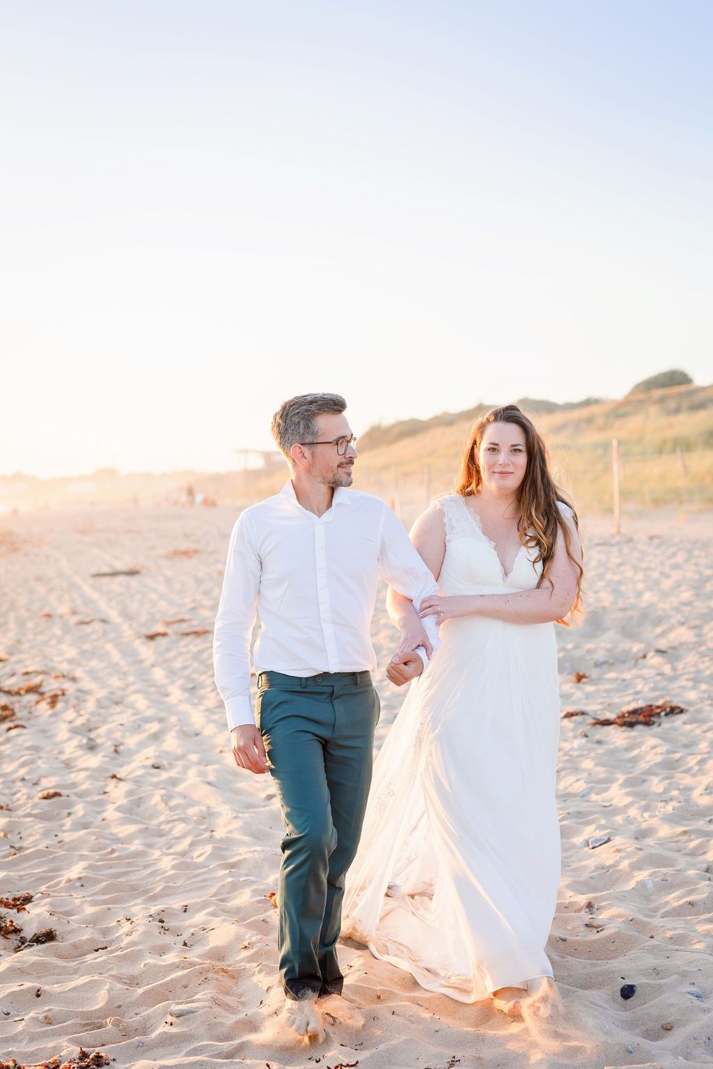 Couple in wedding attire dancing together on sunny beach.