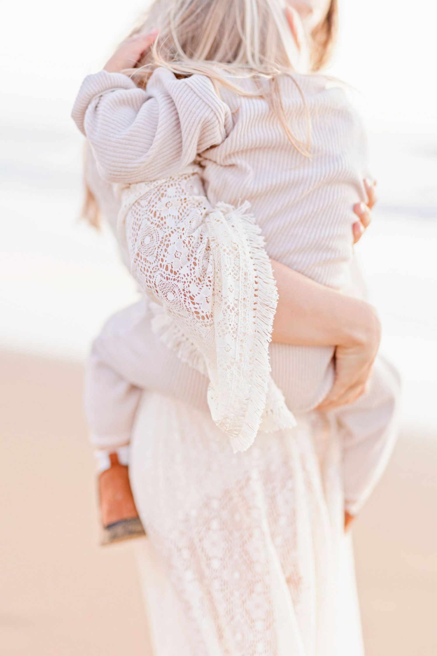 Back view of parent carrying child while wearing matching white outfits on the beach.